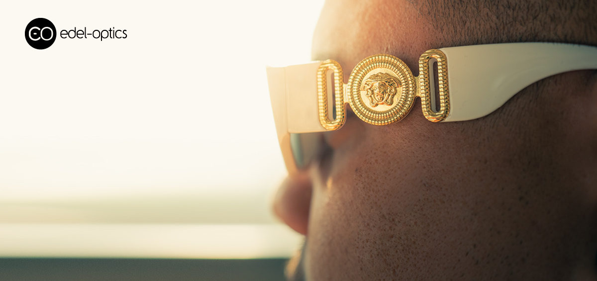 Ein Mann mit einer Sonnenbrille mit goldenem Versace-Logo blickt in den Sonnenuntergang.
